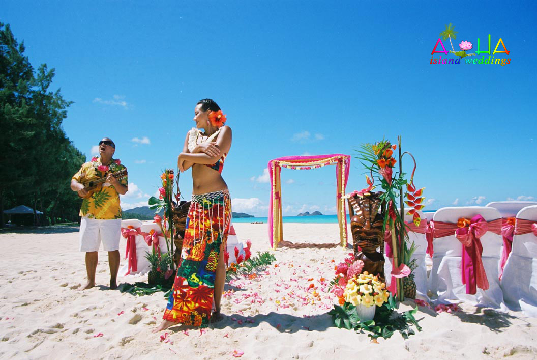 Hula dancer performing at a beach wedding beside a pink and white arch